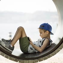 Ein kleiner Junge auf einem Spielplatz hat seinen Blick auf ein Smartphone vertieft.
