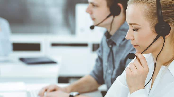 Call center. Group of casual dressed operators at work. Blond business woman in headset at customer service office. Telesales in business
