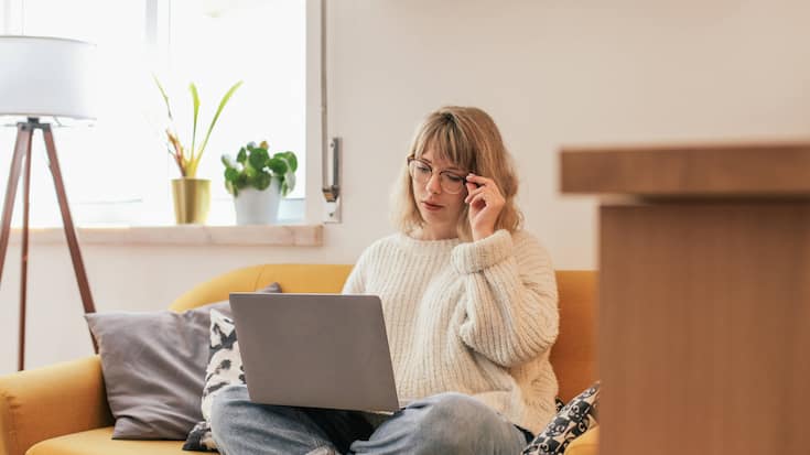 Woman in glasses sitting on a couch and using a laptop