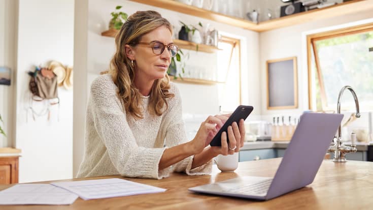 Versicherungsangebot online - Frau mit Handy vor Laptop