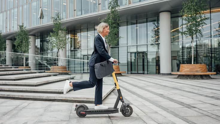 Investition in nachhaltiges Bürogebäude - mit Businesswoman auf E-Scooter