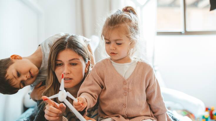 Mother holding wind turbine lying by daughter and son at home