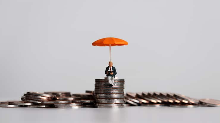 Stack of coins and a miniature people with a orange umbrella.