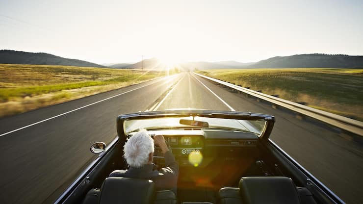Senior man driving convertible car at sunrise