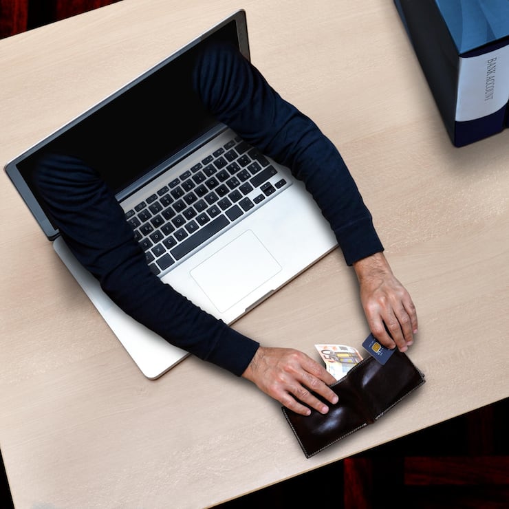 Arme, die aus einem Laptop kommen und Geld stehlen, das auf Bürotisch liegt