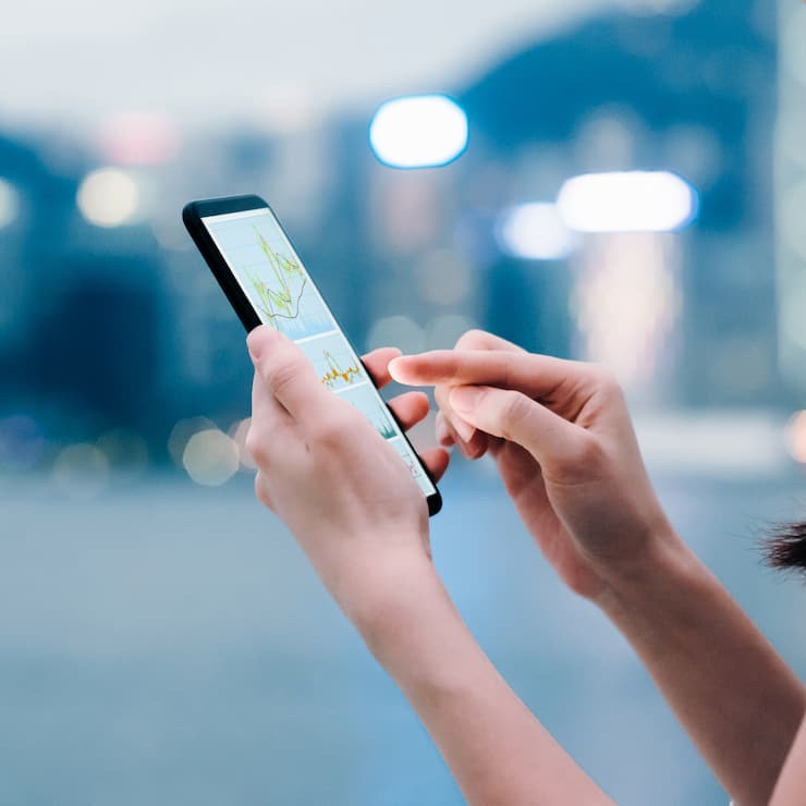 Woman checking financial trading data with smartphone in city