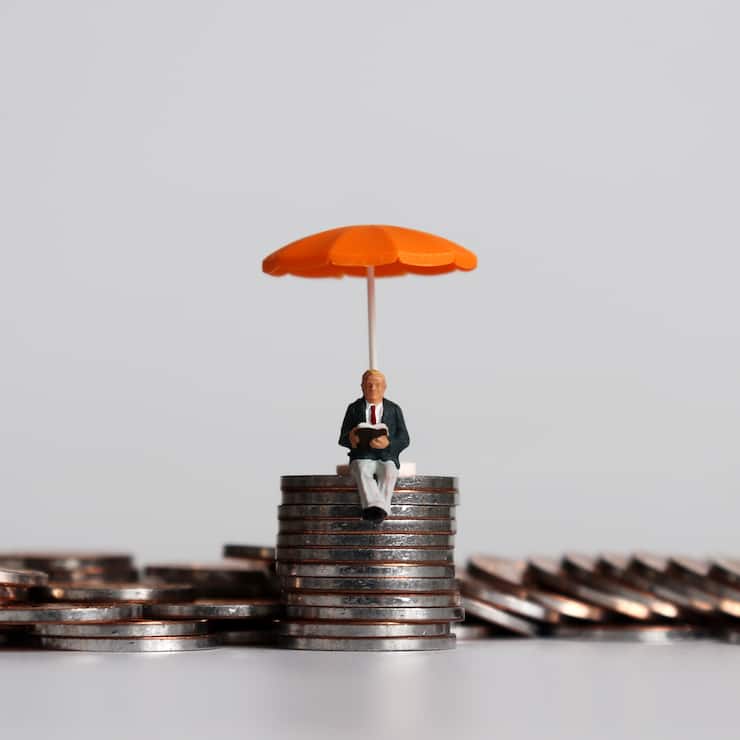 Stack of coins and a miniature people with a orange umbrella.