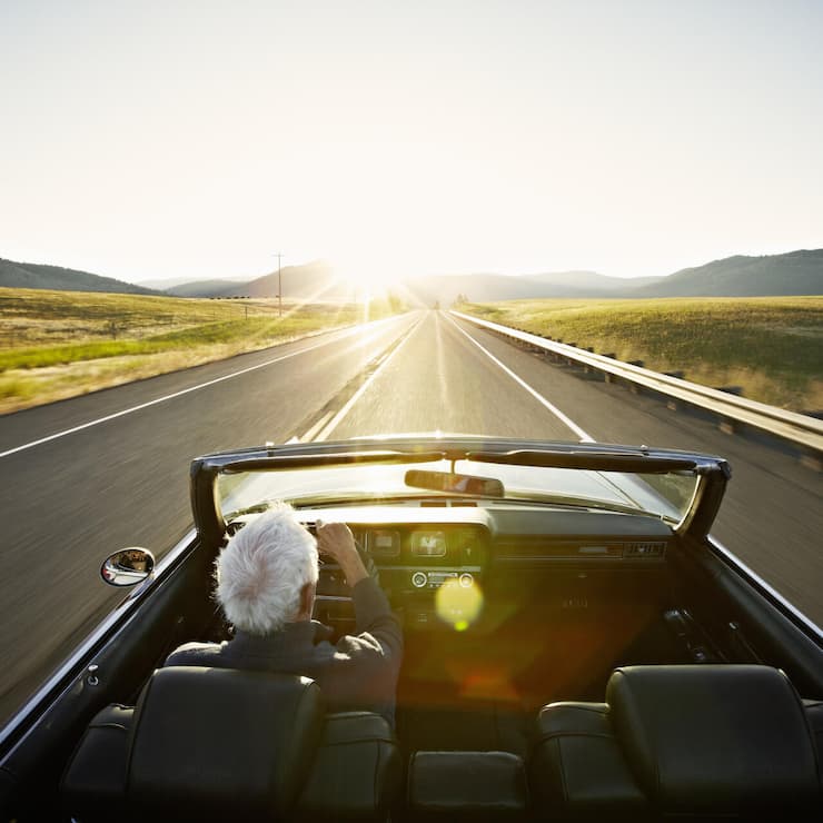 Senior man driving convertible car at sunrise