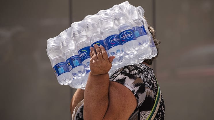 Une femme porte des bouteilles d'eau sur la plage de Malagueta à Malaga, en Espagne, le 19 juillet 2023.