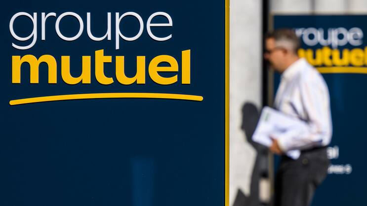 Une personne passe a cote du nouveau logo de la compagnie d'assurance Groupe Mutuel devant le batiment du siege principal le mercredi 21 septembre 2022 a Martigny. La semaine prochaine le Conseil federal doit annoncer le montant des primes des caisses maladie pour l'annee prochaine, une hausse des primes est annoncee. (KEYSTONE/Jean-Christophe Bott)